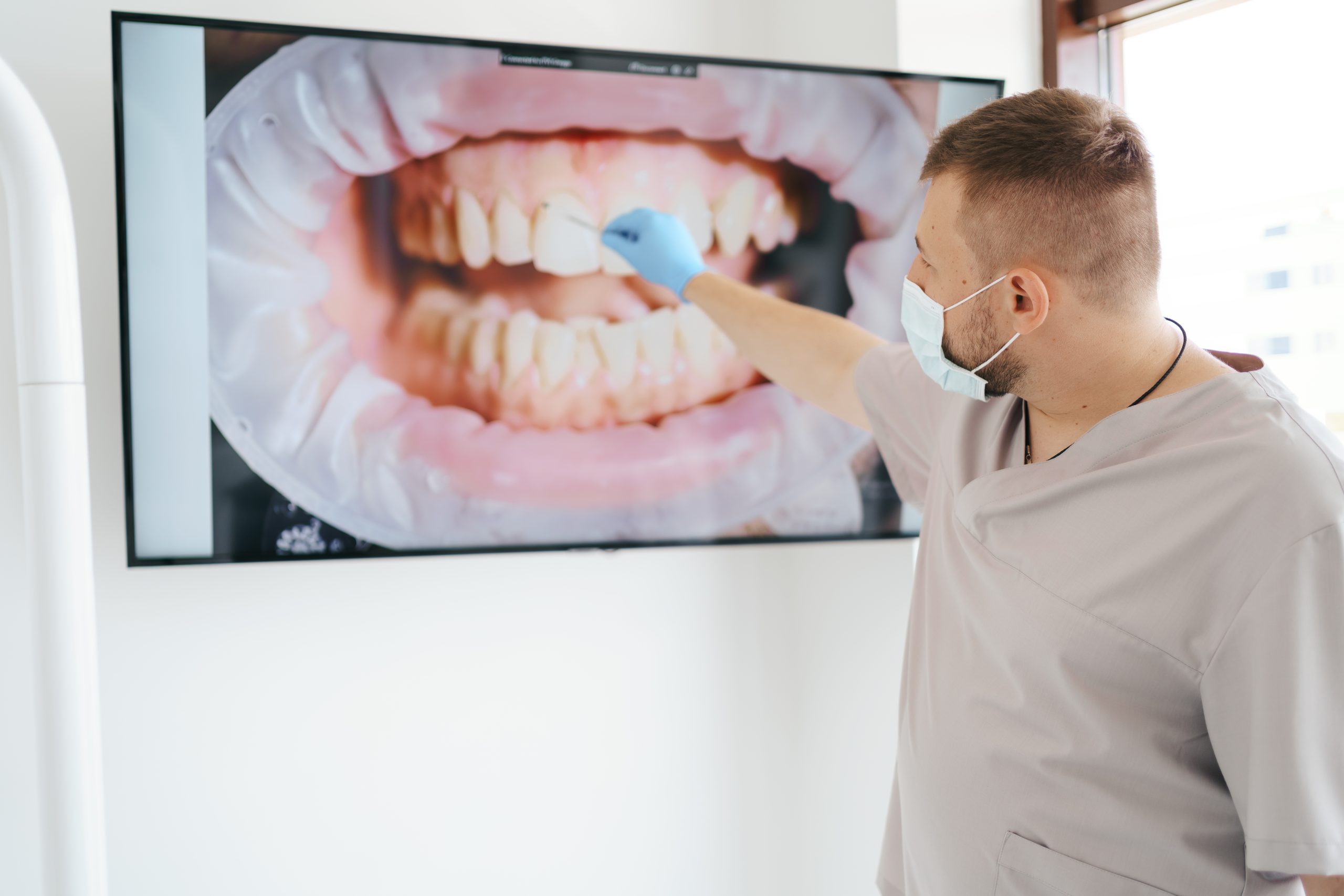 Dentist medical mask pointing patient teeth big screen explaining treatment phases scaled.