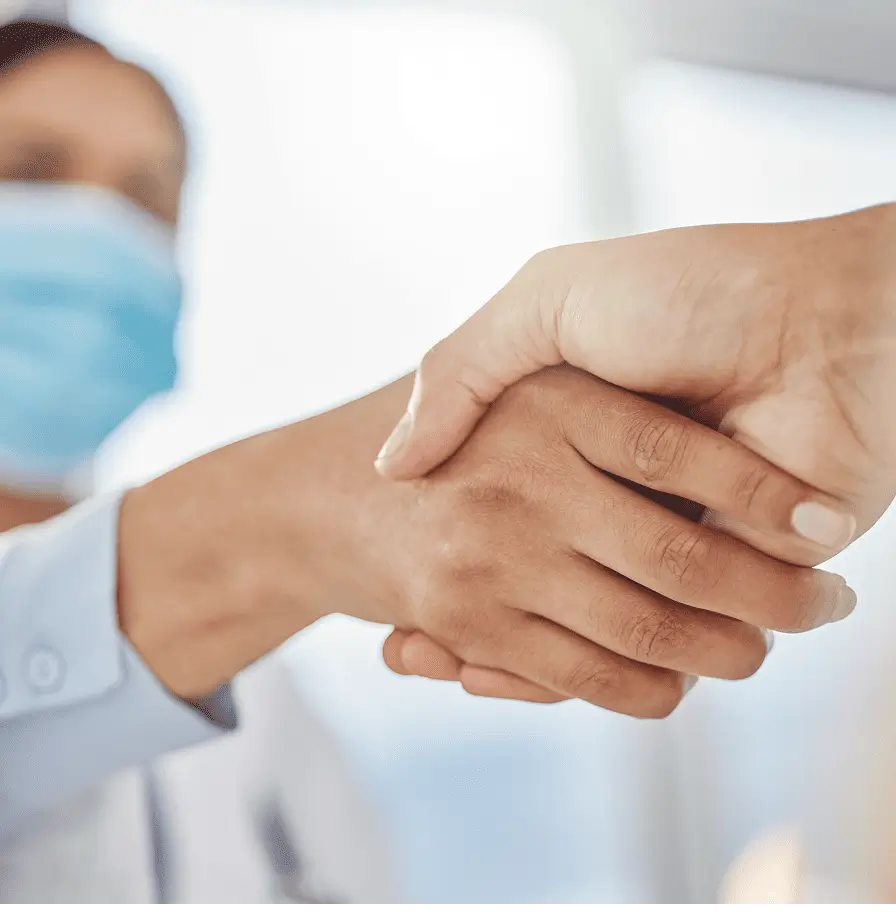 A doctor and another person shaking hands in a professional setting, symbolizing collaboration and agreement.