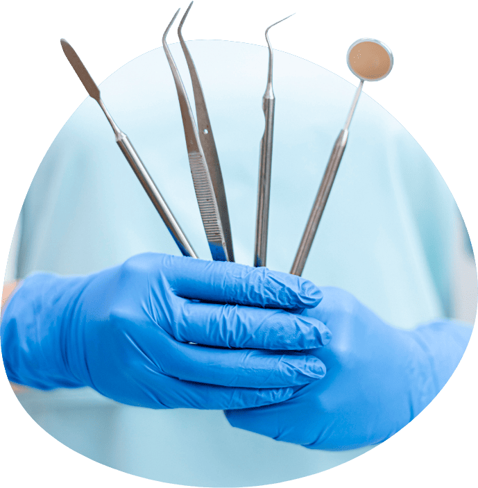 A person wearing blue gloves holds a set of dental tools, ready for a dental procedure.